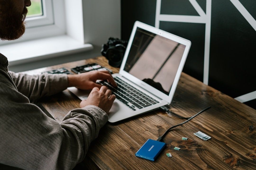 Person arbetar vid laptop med extern hårddisk och minneskort på bordet